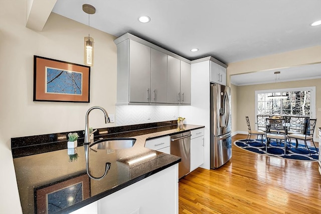 kitchen with decorative light fixtures, a sink, stainless steel appliances, light wood-style floors, and backsplash