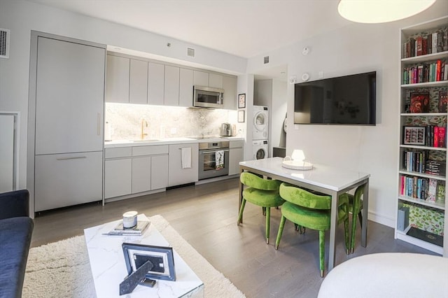 kitchen with light wood-style flooring, stacked washer / dryer, a sink, light countertops, and appliances with stainless steel finishes