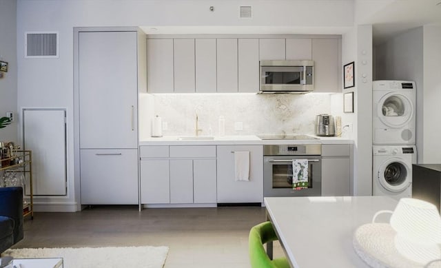 kitchen with stainless steel appliances, a sink, visible vents, stacked washer / drying machine, and light countertops