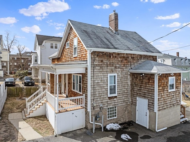 rear view of property with roof with shingles, a porch, a chimney, and fence