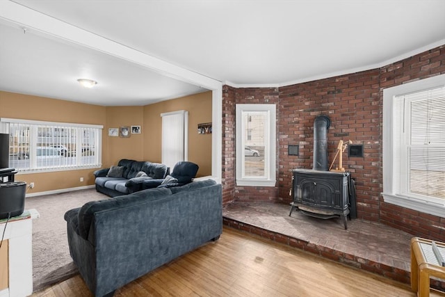 living area featuring a wood stove, brick wall, baseboards, and wood finished floors