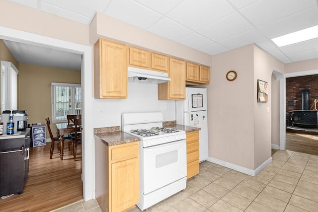 kitchen with a drop ceiling, light brown cabinets, under cabinet range hood, white appliances, and a wood stove