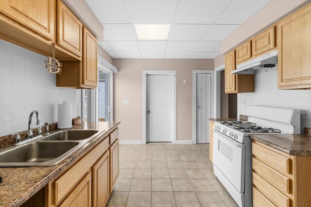 kitchen featuring light tile patterned floors, white range with gas cooktop, tasteful backsplash, under cabinet range hood, and a sink