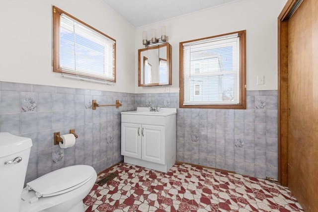 bathroom featuring toilet, wainscoting, tile walls, and vanity