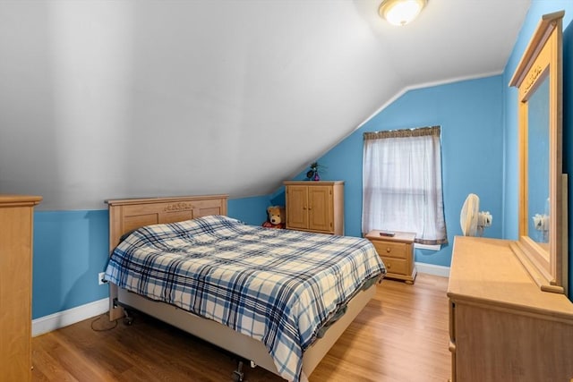 bedroom with baseboards, vaulted ceiling, and light wood finished floors