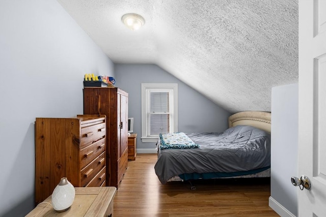 bedroom with vaulted ceiling, a textured ceiling, and wood finished floors