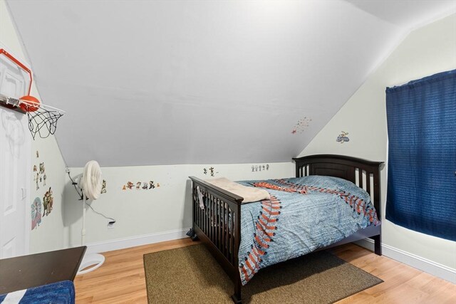 bedroom with vaulted ceiling, wood finished floors, and baseboards