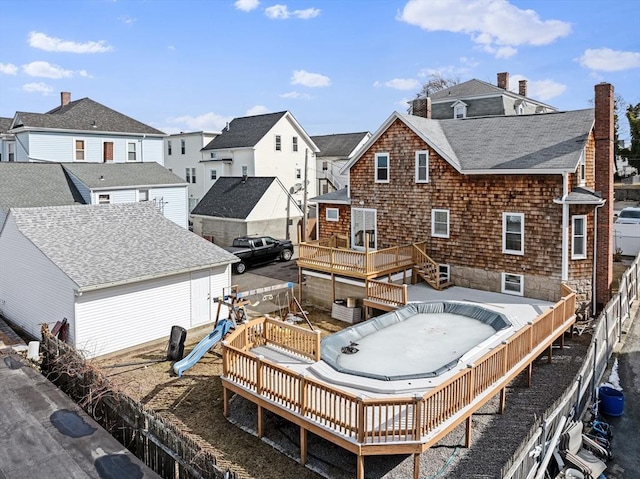 rear view of property featuring a chimney, a shingled roof, fence, a residential view, and a wooden deck