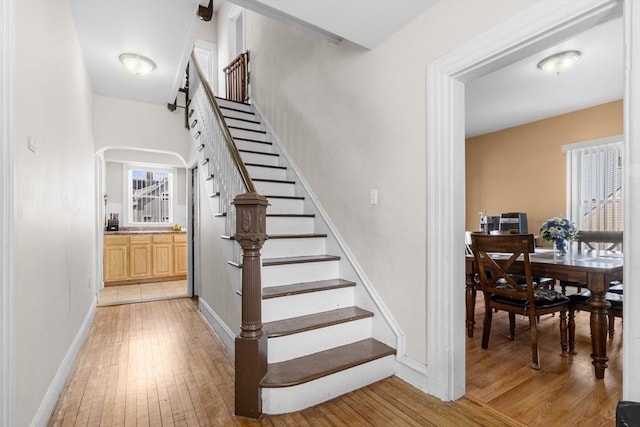 stairs featuring arched walkways, hardwood / wood-style floors, and baseboards