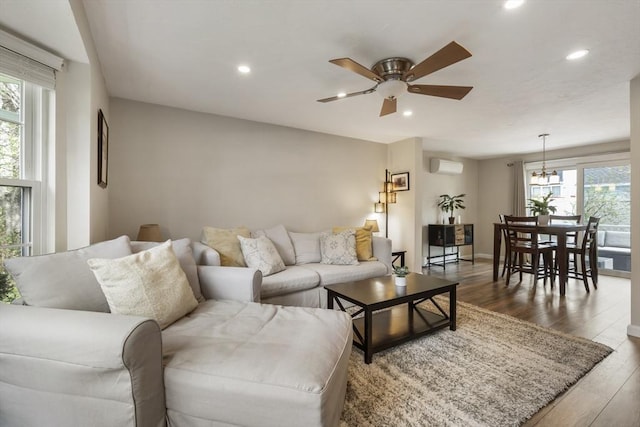 living area featuring an AC wall unit, a wealth of natural light, wood finished floors, and ceiling fan with notable chandelier