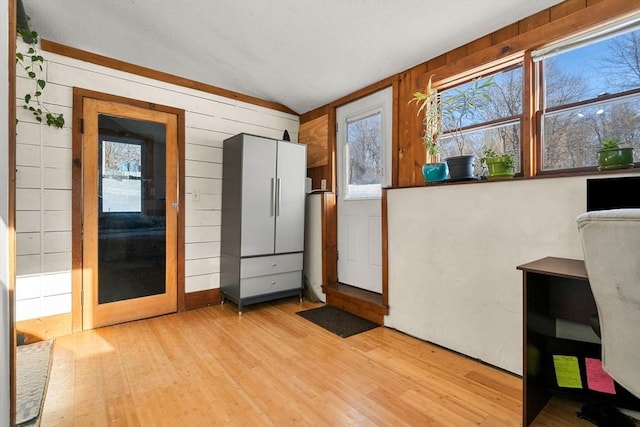 entryway featuring light hardwood / wood-style floors, vaulted ceiling, and wooden walls