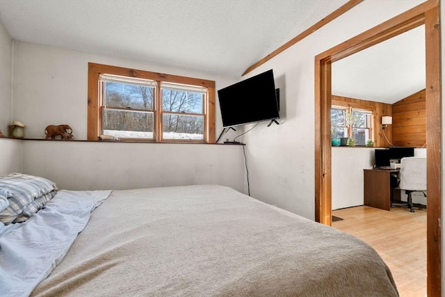 bedroom featuring vaulted ceiling, wood walls, and light hardwood / wood-style floors