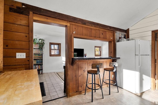 kitchen featuring white fridge, kitchen peninsula, a breakfast bar, vaulted ceiling, and wood walls