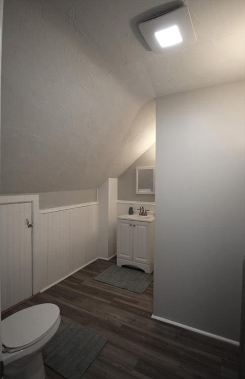 half bathroom featuring toilet, vanity, vaulted ceiling, wood finished floors, and a textured ceiling