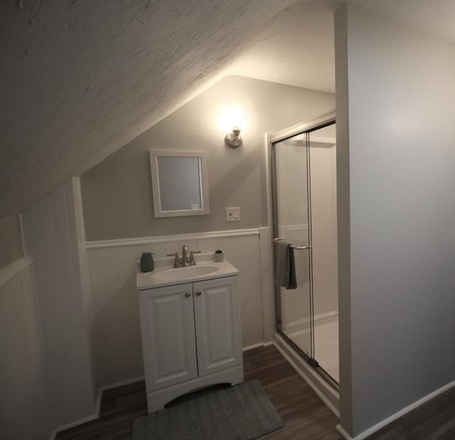 bathroom with vanity, wood finished floors, a wainscoted wall, vaulted ceiling, and a shower stall