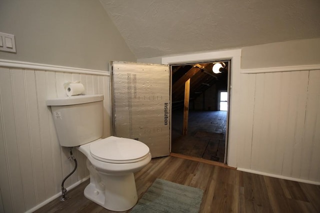 bathroom featuring toilet, vaulted ceiling, wainscoting, wood finished floors, and a textured ceiling