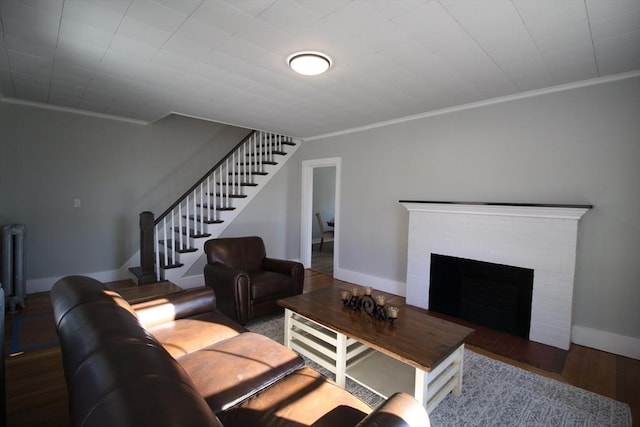 living area with a brick fireplace, crown molding, baseboards, stairway, and wood finished floors