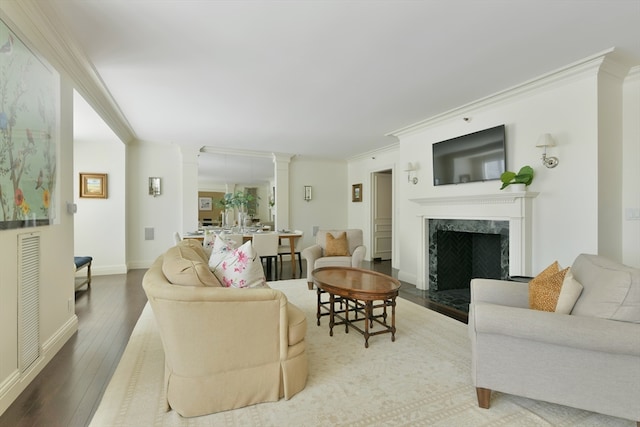 living room featuring wood-type flooring, crown molding, ornate columns, and a high end fireplace