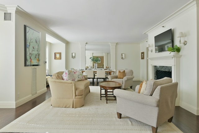 living room with ornamental molding, wood-type flooring, a premium fireplace, and ornate columns