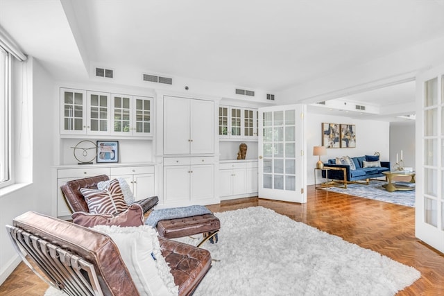 living area featuring french doors, a tray ceiling, and light parquet flooring