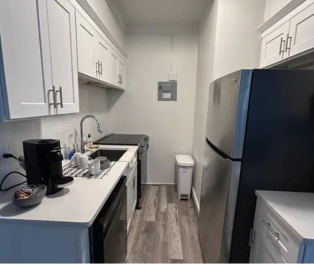 kitchen with white cabinetry, stainless steel refrigerator, black dishwasher, hardwood / wood-style floors, and decorative backsplash