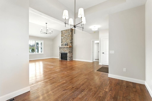 unfurnished living room with baseboards, a chandelier, vaulted ceiling, a fireplace, and wood finished floors