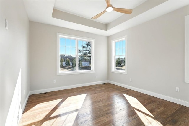 spare room with baseboards, a raised ceiling, wood finished floors, and a ceiling fan