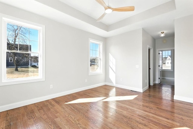 unfurnished room featuring a healthy amount of sunlight, a tray ceiling, baseboards, and wood finished floors