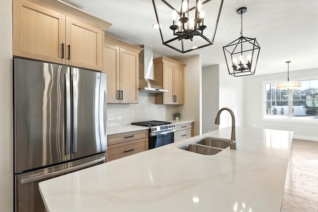 kitchen with light brown cabinets, an inviting chandelier, a sink, appliances with stainless steel finishes, and wall chimney exhaust hood