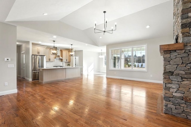 unfurnished living room featuring baseboards, a chandelier, vaulted ceiling, recessed lighting, and light wood-style flooring