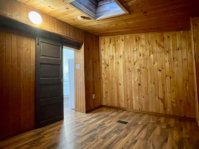 empty room with hardwood / wood-style flooring, wooden walls, a skylight, and wooden ceiling