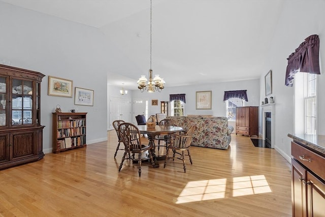 dining area featuring a fireplace with flush hearth, baseboards, light wood-type flooring, and an inviting chandelier