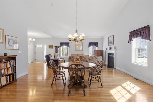 dining area with baseboards, high vaulted ceiling, a fireplace, a notable chandelier, and light wood-type flooring