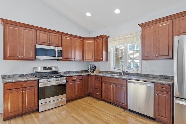 kitchen with light wood-style flooring, a sink, dark countertops, appliances with stainless steel finishes, and vaulted ceiling