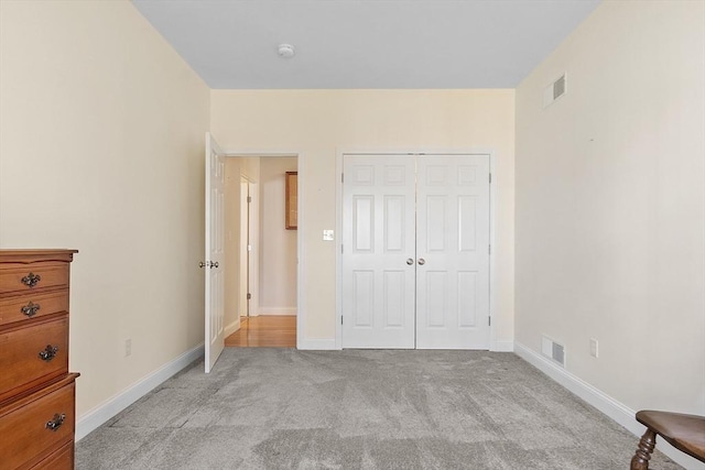 unfurnished bedroom featuring visible vents, baseboards, light colored carpet, and a closet