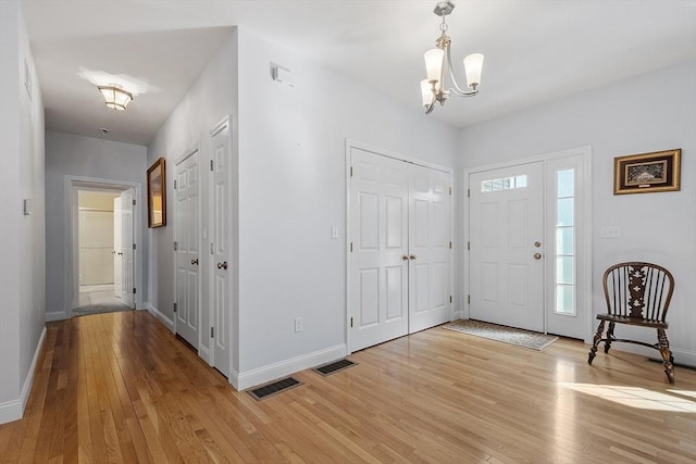 entryway featuring light wood-type flooring, baseboards, a notable chandelier, and visible vents