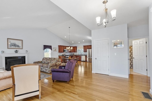 living room with visible vents, a glass covered fireplace, light wood-style floors, lofted ceiling, and a chandelier