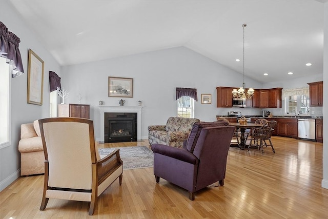 living room featuring baseboards, a chandelier, light wood-type flooring, lofted ceiling, and a glass covered fireplace