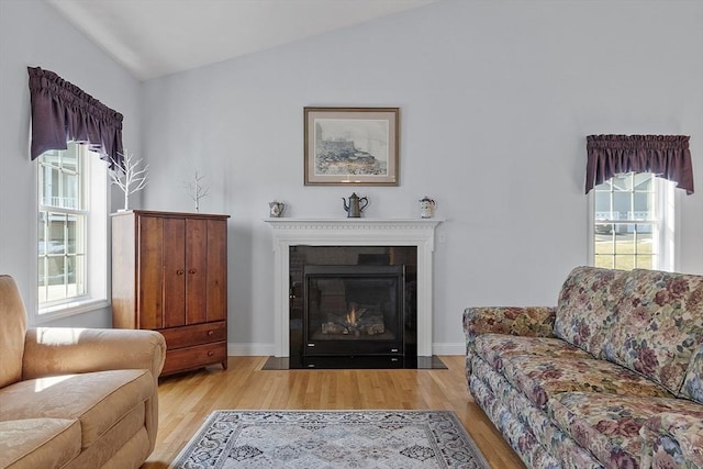 living room with a wealth of natural light, a fireplace with flush hearth, lofted ceiling, and wood finished floors