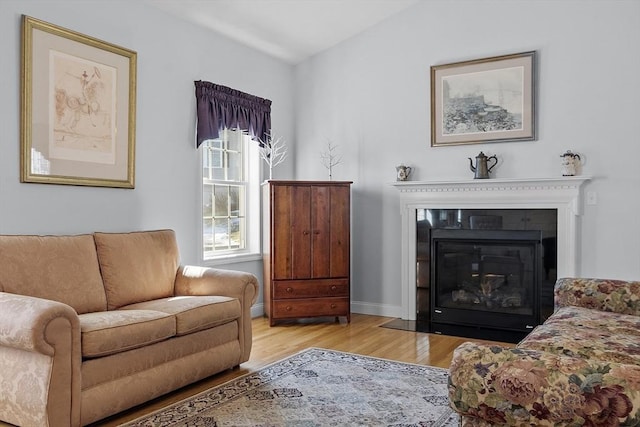 living area with vaulted ceiling, a fireplace with flush hearth, wood finished floors, and baseboards