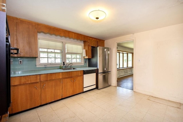 kitchen featuring dishwasher, a sink, freestanding refrigerator, brown cabinetry, and a baseboard heating unit