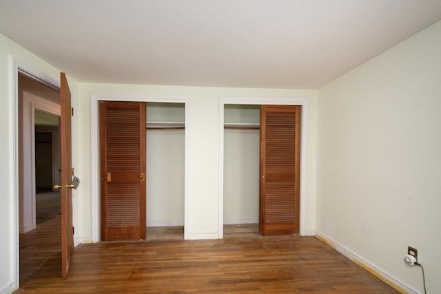 unfurnished bedroom with multiple closets, wood finished floors, and baseboards