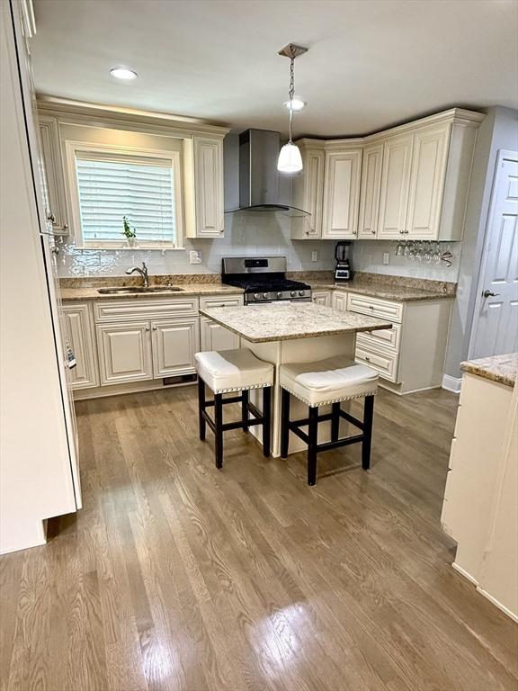 21 Florence Ave, Lowell, MA 01851 - kitchen featuring stainless steel gas stove, wall chimney exhaust hood, a sink, pendant lighting, and wood finished floors