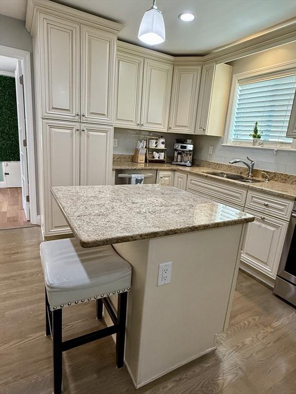 21 Florence Ave, Lowell, MA 01851 - kitchen with a sink, a kitchen island, wood finished floors, light stone counters, and a kitchen bar