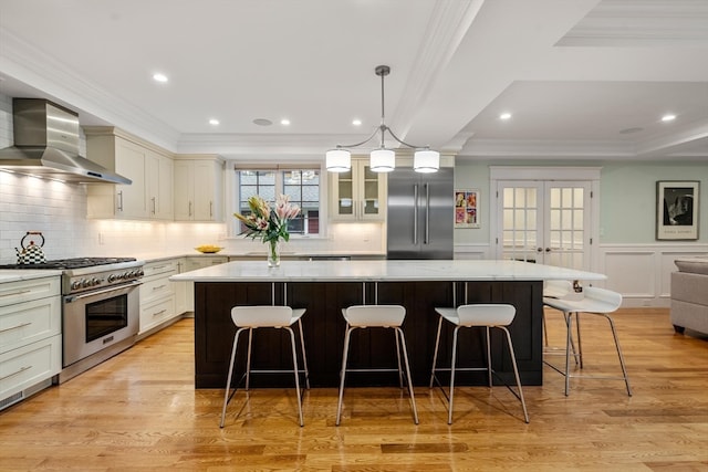 kitchen with light wood-type flooring, a kitchen island, wall chimney range hood, and high quality appliances