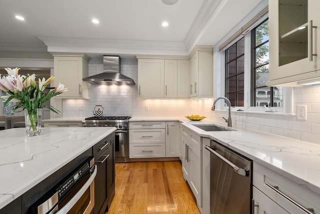 kitchen featuring sink, wall chimney range hood, stainless steel appliances, light stone countertops, and decorative backsplash