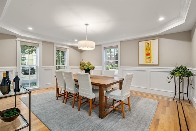 dining room with light wood-type flooring, crown molding, a raised ceiling, and a healthy amount of sunlight