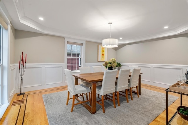 dining room with light hardwood / wood-style flooring, a tray ceiling, and ornamental molding