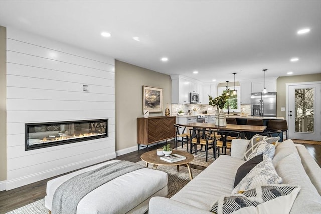 living room featuring dark wood-style floors, baseboards, a large fireplace, and recessed lighting