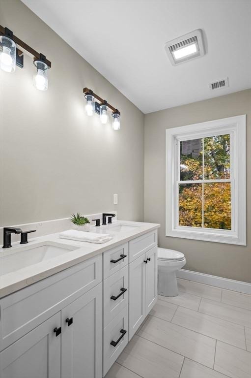 bathroom featuring visible vents, a sink, toilet, and double vanity